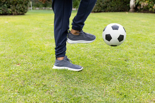 African American man in navy track pants, gray sneakers controlling soccer ball in yard, copy space