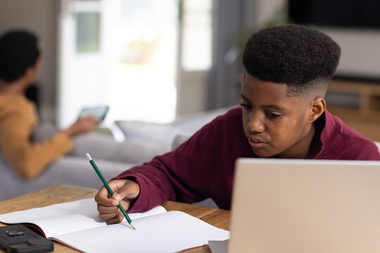 African father and teen son studying at home at wooden table with laptop notebook pencil tablet