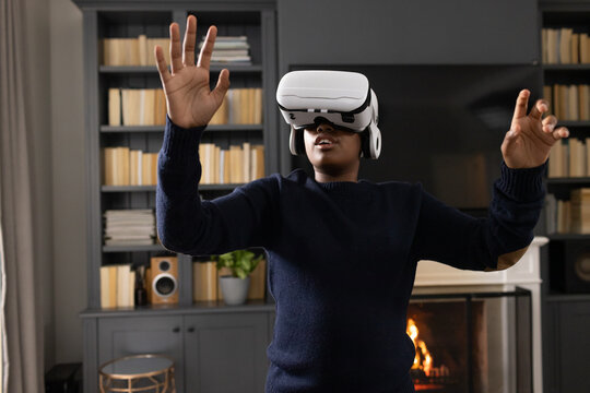 African American man standing wearing navy sweater and white VR headset reaching toward fireplace