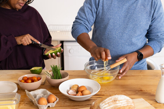 African American couple preparing meal at home kitchen, cracking eggs into glass mixing bowl