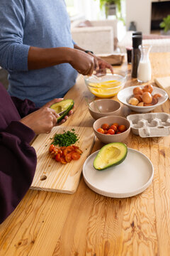 African American couple whisking eggs and halving avocado at kitchen counter with cutting board