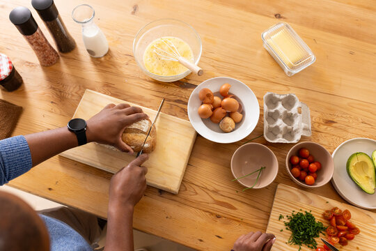 African couple slicing bread, arranging herbs on cutting boards in kitchen, smartwatch, copy space