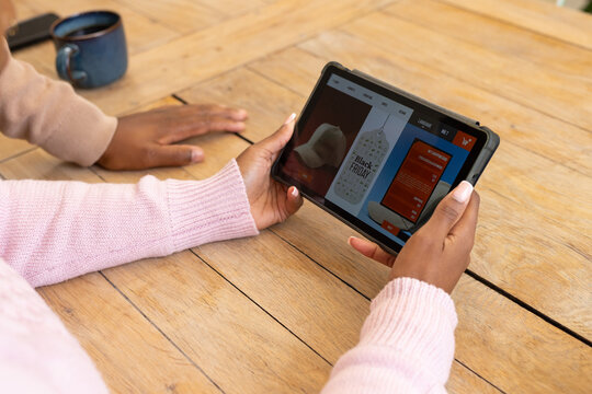 African American couple shopping Black Friday on tablet at wooden table with blue mug wearing knits