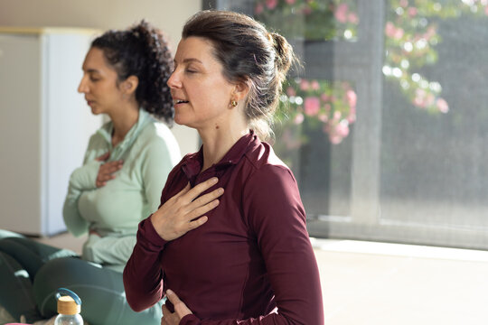Diverse female classmates doing breathwork on mats in studio wearing tops with bottle, copy space