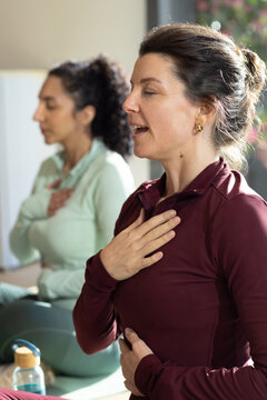 Female participants practicing calm breathwork on green yoga mats in home studio with water bottle