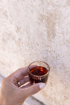 female hand holding a shot of Ginja - portugese cherry liqueur against a textured wall, copy space