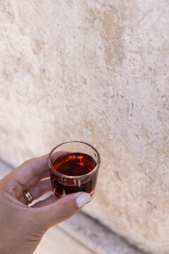 female hand holding a shot of Ginja - portugese cherry liqueur against a textured wall, copy space