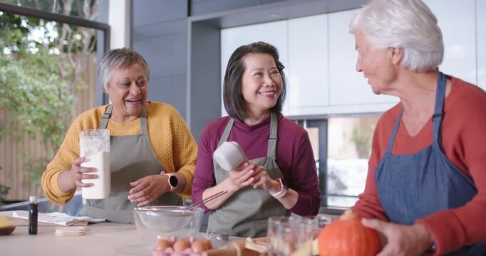 Diverse female friends starting baking, scooping flour, inspecting measuring cups at kitchen island
