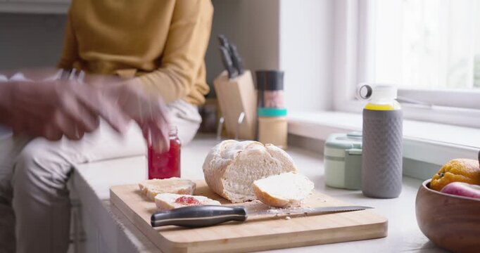 African family dad and teen, dad entering, spreading jam on bread for snack at kitchen counter