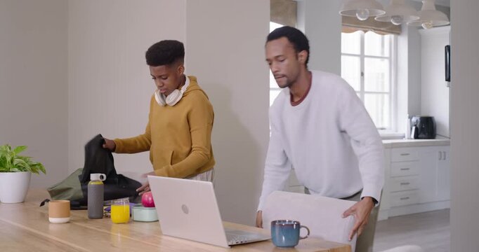 African American dad and teen exchanging look packing backpacks laptop and headphones leaving table