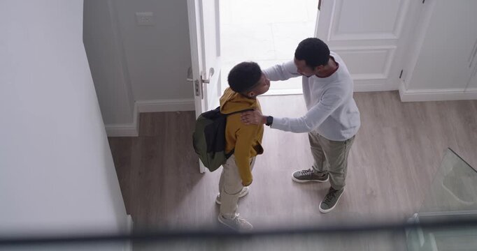 African American father approaching teen preparing to leave at open door, adjusting green backpack
