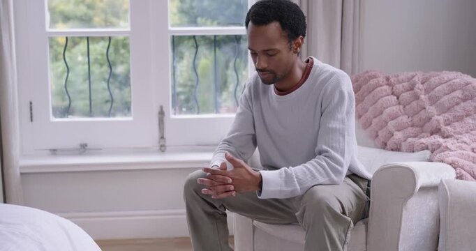 African American man sitting on chair by window, fidgeting with glasses, preparing to meet camera