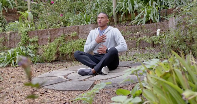 African American man meditating on stone slab in garden, starting hands chest belly, camera panning
