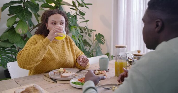 African American couple, woman in yellow top raising orange juice talking man eating toast at table