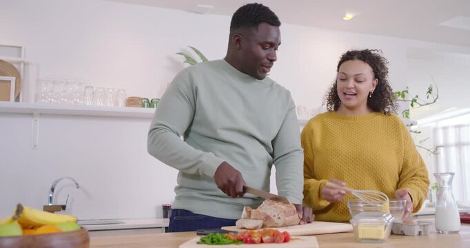 African American couple starting prep at island, man slicing bread on board as woman whisking eggs