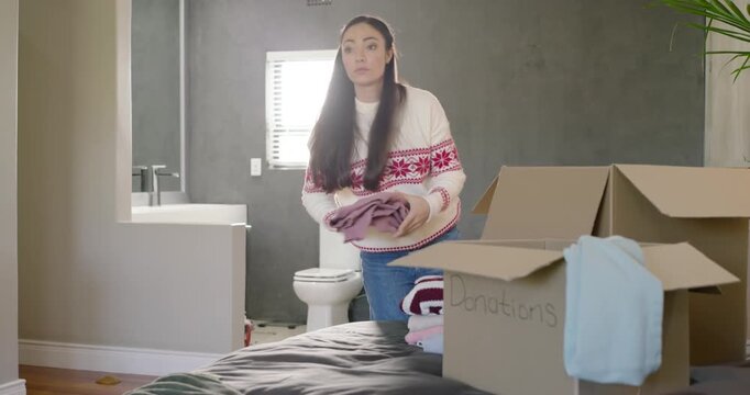 Woman finding pile in bedroom, inspecting, folding and packing clothes into Donations box to donate