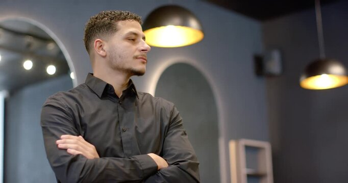 Camera moving closer, man standing arms crossed turning head to camera smiling in studio mirror
