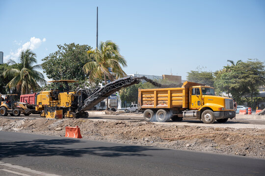 Caterpillar PM622 cold planer, by Caterpillar Inc., milling pavement and loading a dump truck at a road construction site. Colima, Mexico, July 20, 2026.