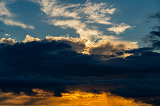 Dramatic sunset sky with dark storm clouds and golden sun rays. Beautiful sunset sky featuring dramatic dark storm clouds, golden sunlight bursts, and light wispy cirrus clouds above