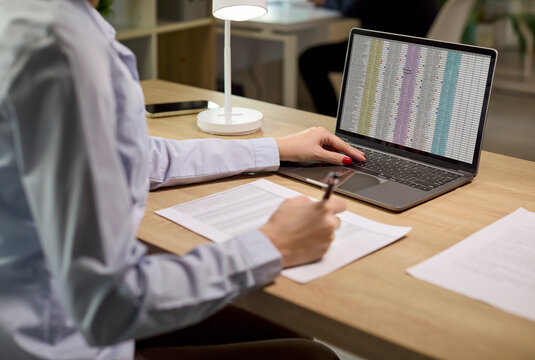 Woman accountant in office with laptop spreadsheet. She reviews spreadsheet data on laptop checks reports, verifies figures, budget, credit risk and compliance. Clear concept of audit and finance.