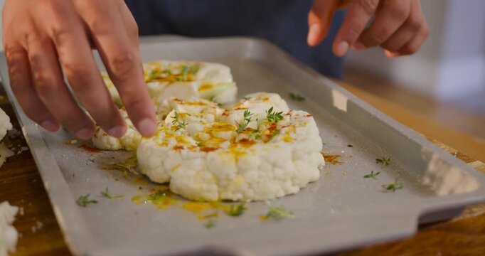After oil drizzle, African American woman arranging cauliflower pieces on pan in kitchen to roast