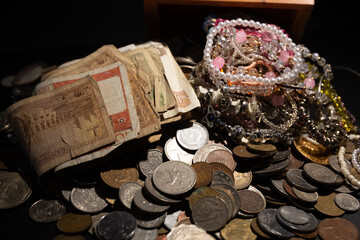 Vintage banknotes and antique coins piled with assorted jewelry on a dark background © saad