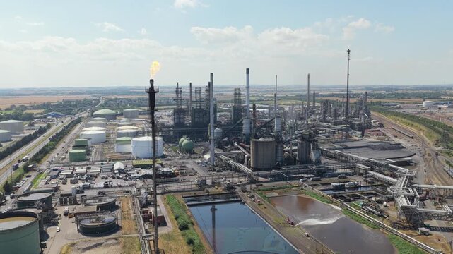 Industrial Oil Refinery With Burning Flare Stack and Storage Tanks in Daylight