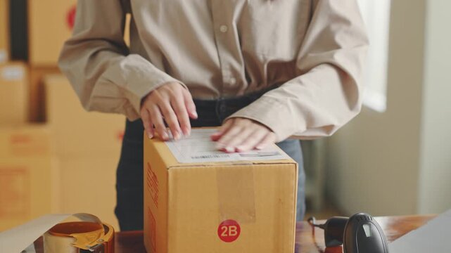 Woman labels a box with shipping sticker and barcode scanner nearby