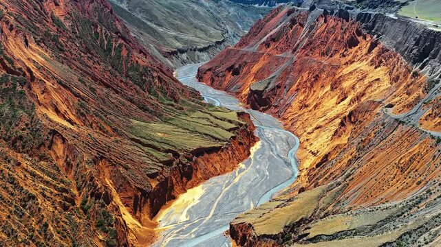 Aerial view of Anjihai Grand Canyon with vibrant red cliffs and a winding river bed, Xinjiang, China.