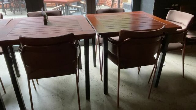 Sequence captured from low indoor viewpoint showing two adjacent varnished wooden tables with slatted tops and surrounding upholstered chairs in foreground