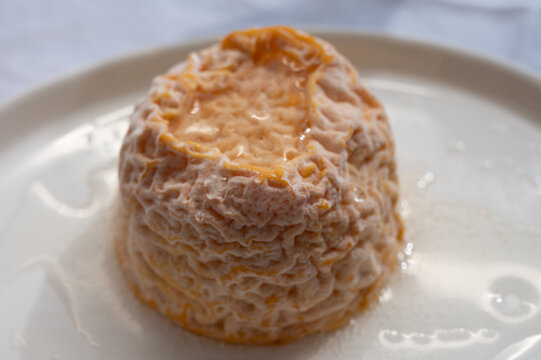 Small, round Langres cheese with orange washed rind and creamy center on a board, spooned and paired with Champagne