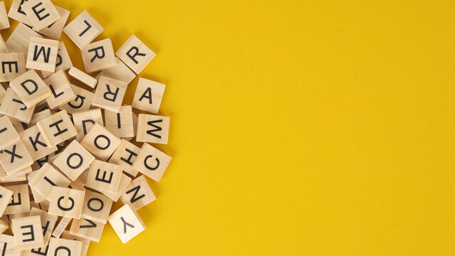 Scattered Wooden Letter Tiles on Yellow Background .