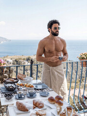 Fototapeta premium Man enjoying breakfast on a balcony overlooking the sea, wearing a towel and sunglasses, isolated on transparent background