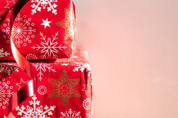 Stacked Christmas gifts wrapped in red festive paper with snowflakes and ribbon on a pink background with copyspace