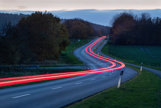 Lichtstreifen eines vorbeifahrenden Fahrzeugs auf einer kurvigen Landstra&szlig;e in der D&auml;mmerung.