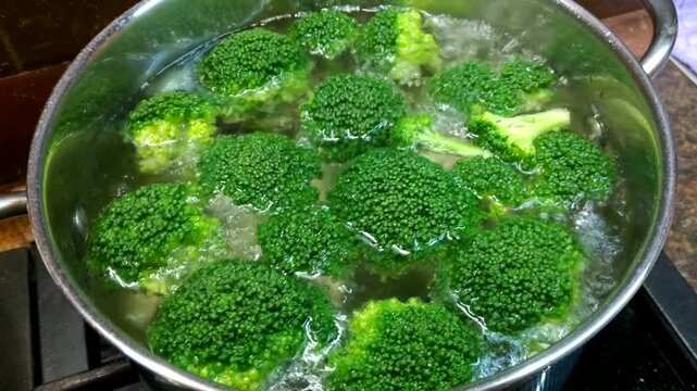 A metal pot of boiling water containing bright green broccoli florets sits on the stove, conveying the impression of a fresh and healthy cooking process.