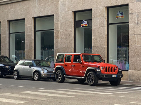 Mini Cooper and Jeep Wrangler parked on Corso Campi street in Cremona, Italy, in front of a dm store