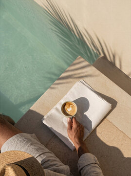 Person enjoying a coffee while sitting by a poolside