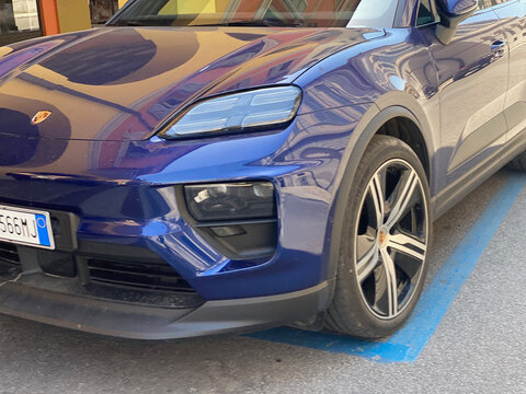 Porsche Macan electric SUV parked on a blue marked spot, highlighting its blue body, headlights, and front wheel