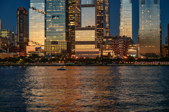 New York, USA, 8 June 2026 : Hudson Yards architecture, close view of buildings and the Vessel. A small boat passes the illuminated skyline and copper structure.