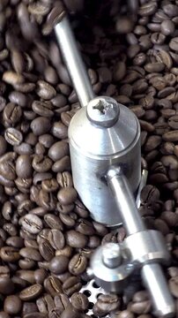 Close-up of roasted coffee beans being stirred and cooled by a rotating metal agitator inside industrial roasting equipment