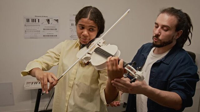 African American teenager practicing violin while Caucasian young male teacher guides her hand placement. Video for promoting music schools and private tutoring services