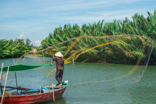 Vietnamese fisherman casting a large yellow net from a traditional wooden boat