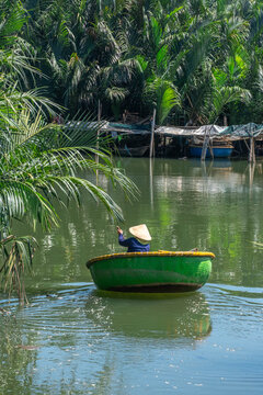 Vietnamese woman paddling a traditional round basket boat down a tropical river channel