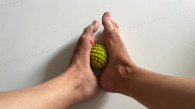 Woman massaging her foot sole with a yellow spiky massage ball