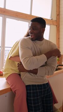 Joyful interracial couple hugging and laughing in the kitchen