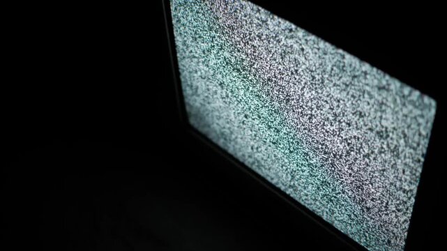 A glowing television monitor displays chaotic static white noise against a pitch-black background. Concept of signal loss, horror movie atmosphere, and retro technology malfunction.