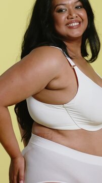 Vertical video: Posing model smoothing underwear while camera panning in studio, showing white bra