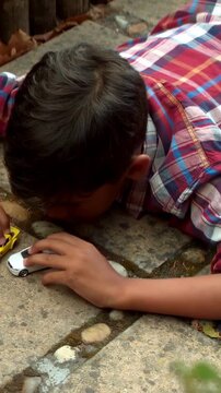 Vertical video: Examining white car, boy in plaid tee pushing yellow car on pavement, aligning cars