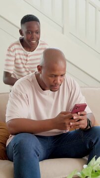 Vertical video: Descending son gifting green Fathers Day card home, dad in pink tee opening hugging